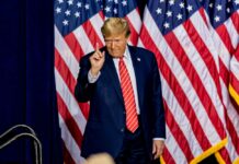 Man standing before American flags wearing suit and tie