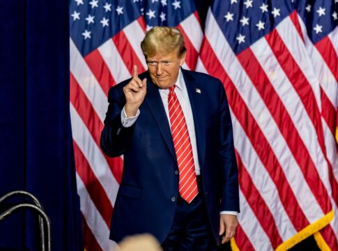 Man standing before American flags wearing suit and tie