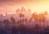 Los Angeles skyline with palm trees at sunset.