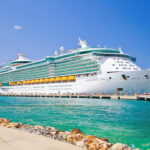 Large cruise ship docked near turquoise water and foliage.