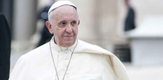 Man in white religious robe and cap outdoors.