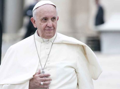 Man in white religious robe and cap outdoors.