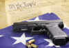 Gun and bullets on American flag with Constitution background.