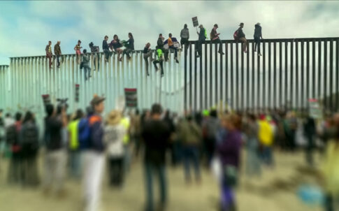 Crowd and people climbing large border wall during protest.