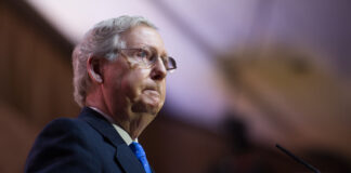 Man in glasses speaks at podium.