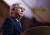 Man in glasses speaks at podium.