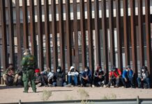 Border patrol agent with group of seated immigrants.