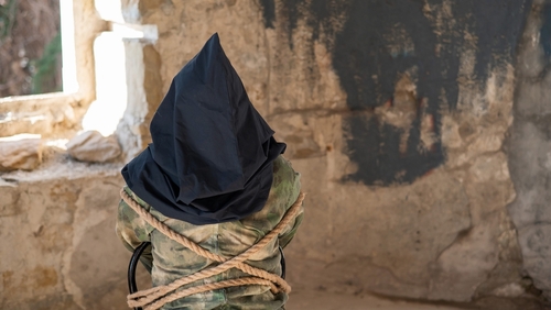 Person hooded and bound in abandoned stone room.