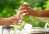 Hands passing a water bottle outdoors, lush green background.