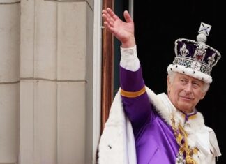 King Charles III in coronation attire waving.