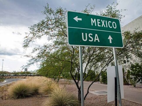 Direction sign for Mexico left, USA straight ahead.