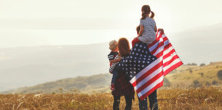 Family holding American flag in a field.