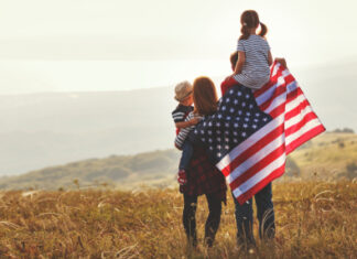 Family holding American flag in a field.