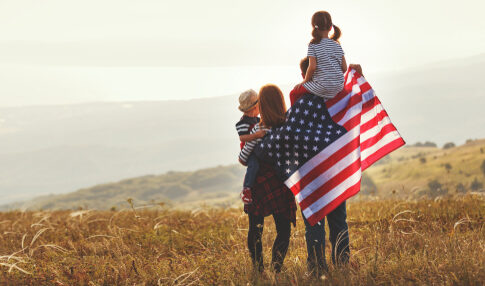 Family holding American flag in a field.