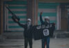 Two masked individuals with a weapon and ISIS flag.