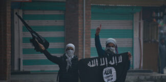 Two masked individuals with a weapon and ISIS flag.