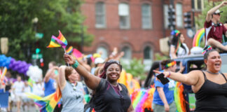 People celebrating at a pride parade, waving rainbow flags.