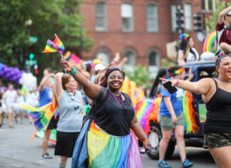 People celebrating at a pride parade, waving rainbow flags.