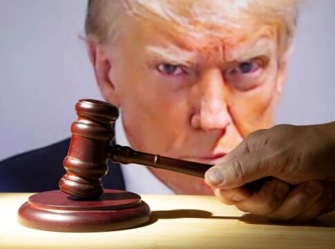 Gavel in foreground, Donald Trump in background, serious expression.