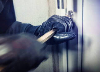 Person breaking into door with crowbar and gloves.