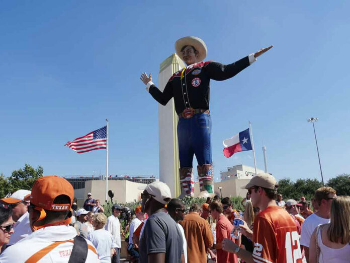 744408097 Giant cowboy statue surrounded by crowd, American and Texas flags.
