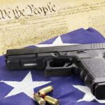 Gun and bullets on American flag with Constitution background.