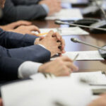 Business meeting participants with hands clasped at a conference table with microphones
