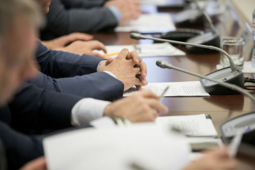 shutterstock1449056195jpg Business meeting participants with hands clasped at a conference table with microphones