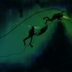 Two scuba divers follow a guideline through a dark underwater cave