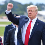 A political figure raising a fist in a gesture of confidence during an outdoor event
