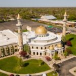 Aerial view of a mosque with golden domes and minarets surrounded by greenery