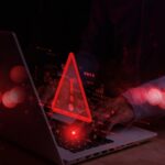 A person typing on a laptop with a red warning symbol overlay