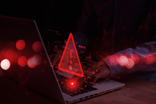 A person typing on a laptop with a red warning symbol overlay