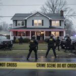 FBI agents at a crime scene outside a house with police vehicles and caution tape