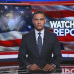News anchor presenting a report in front of an American flag backdrop
