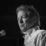 SHOCKING Antisemitic Conspiracy Tirade Rocks Capitol Hill… A man with curly hair speaking into a microphone in black and white