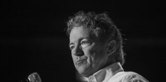 A man with curly hair speaking into a microphone in black and white