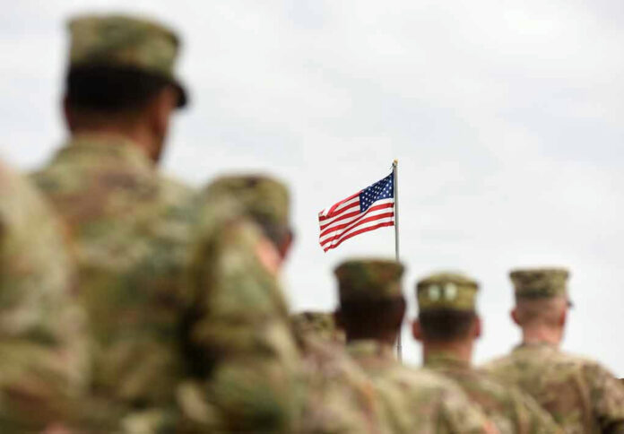 1170998920 Soldiers in uniform standing, American flag in background.