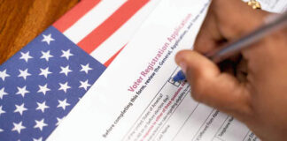 Person filling out voter registration form, American flag background.
