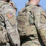 Soldiers in camouflage uniforms with American flags on sleeves.