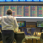 Person viewing stock market data on multiple screens.
