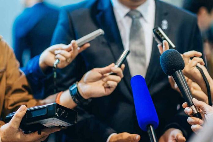 471987565 Journalists holding microphones interview a person in a suit.