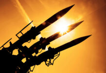 Silhouetted missiles on a launcher against a bright sunset sky