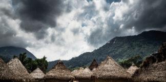 A rural village with thatched huts set against a mountainous backdrop under a cloudy sky