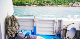 A man lying on the deck of a boat surrounded by fishing ropes with a view of the ocean