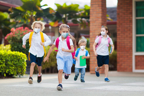 shutterstock_1736145332 Children wearing masks running outside a school