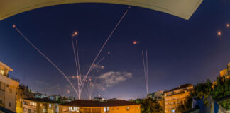 Night sky with missile defense system intercepting rockets above city.