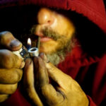 Person igniting a pipe, wearing a red hoodie.