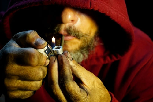 Person igniting a pipe, wearing a red hoodie.