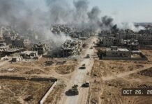 Aerial view of a war-torn city with smoke rising from buildings